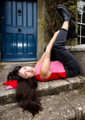Woman lying on a stone steps wearing a red and pink sleeveless top with a blue door in the background