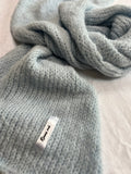 Grey knitted scarf with a brand tag on a light background